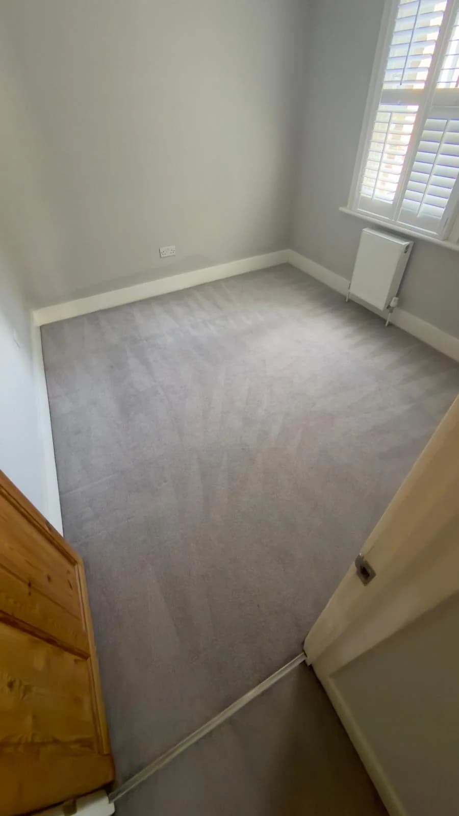Grey fitted room carpet viewed from the wooden doorway, with cleaning passes across the pile.