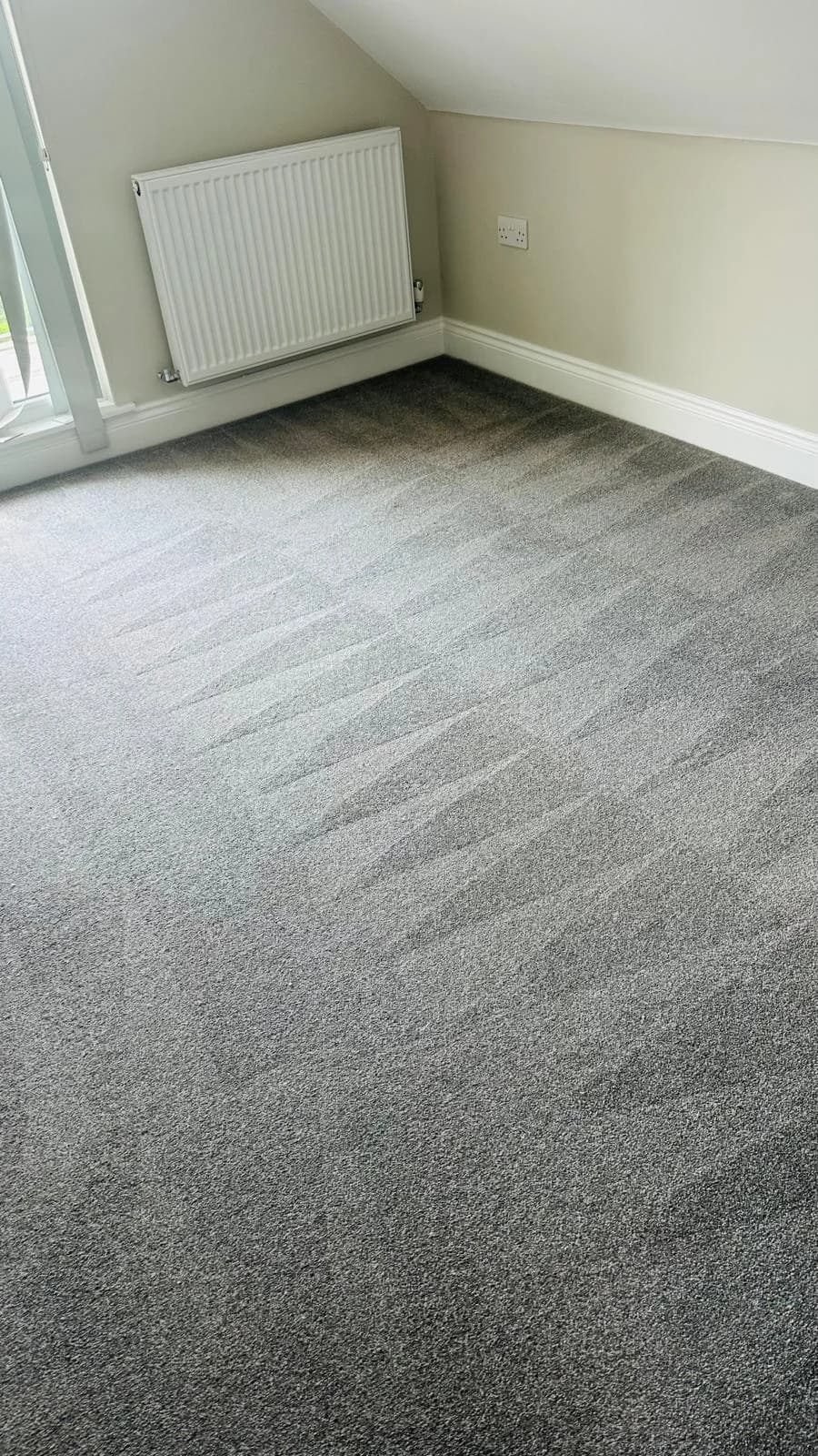 Grey bedroom carpet beside a bright window, showing the texture of the pile in a OneGo Cleaning Masters work photo.