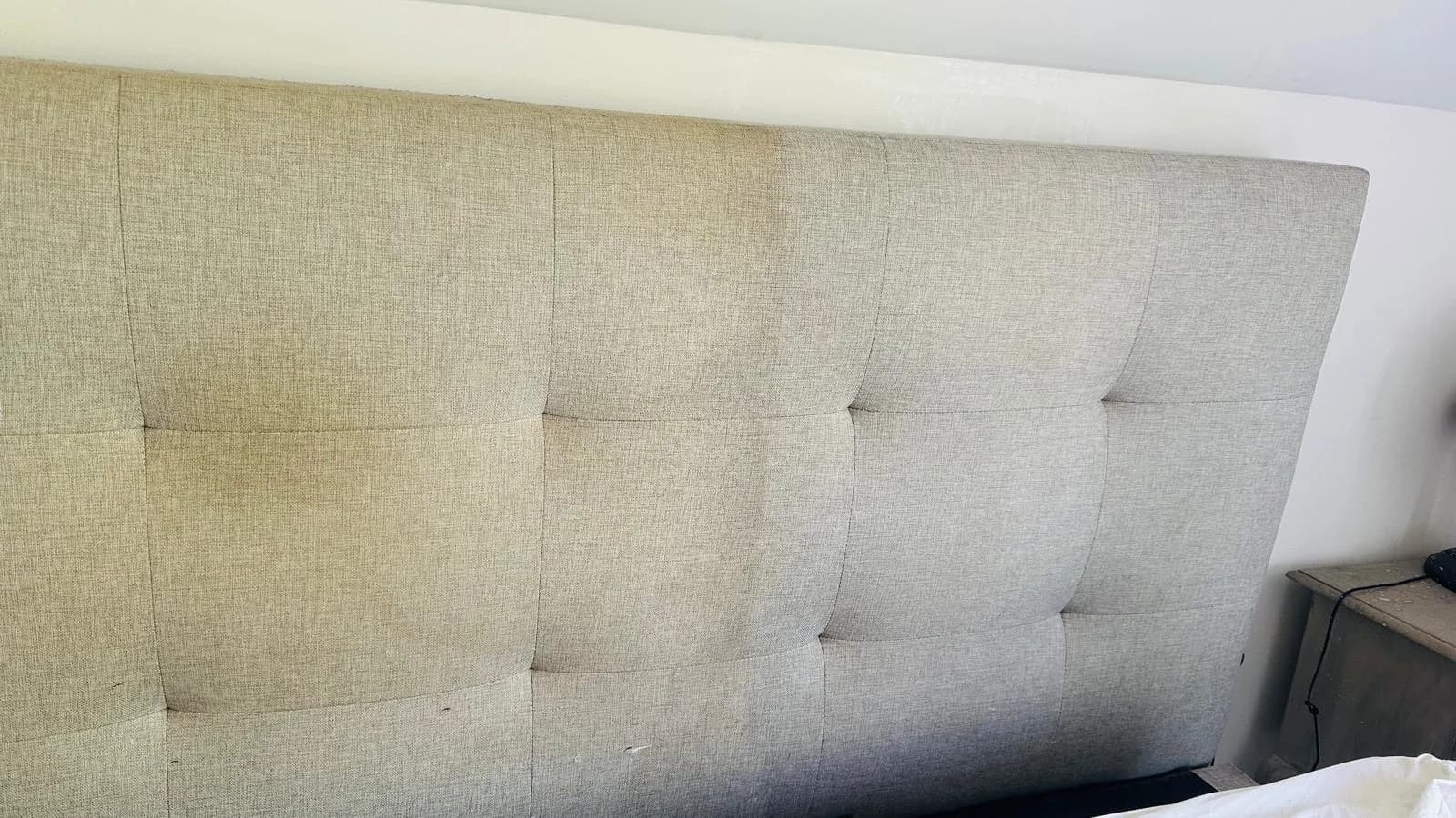 Close view of a light fabric headboard with button tufting, photographed during OneGo Cleaning Masters upholstery work.